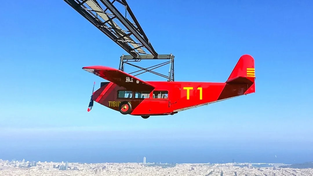 Red airplane ride at Tibidabo Amusement Park with Barcelona cityscape below.