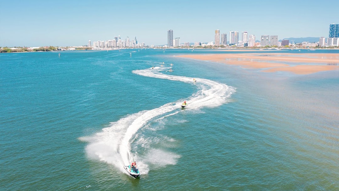 Jet skis creating trails on blue water with city skyline in the background.