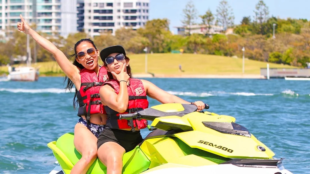 Jet ski riders enjoying a water adventure near cityscape backdrop.