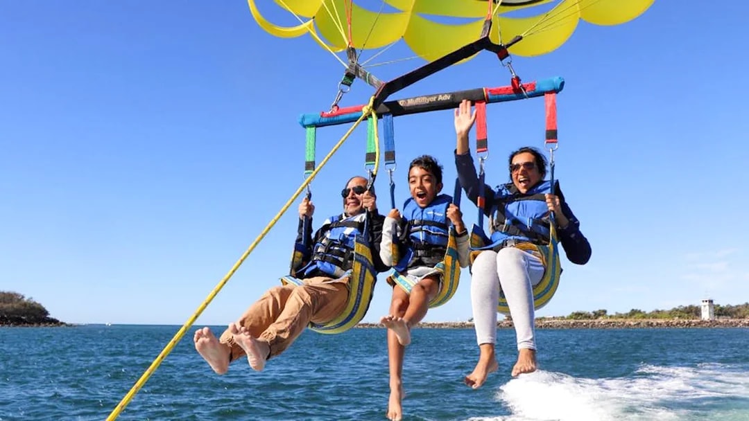 Parasailing over ocean with three people enjoying the Jet Ski & Parasail Experience.