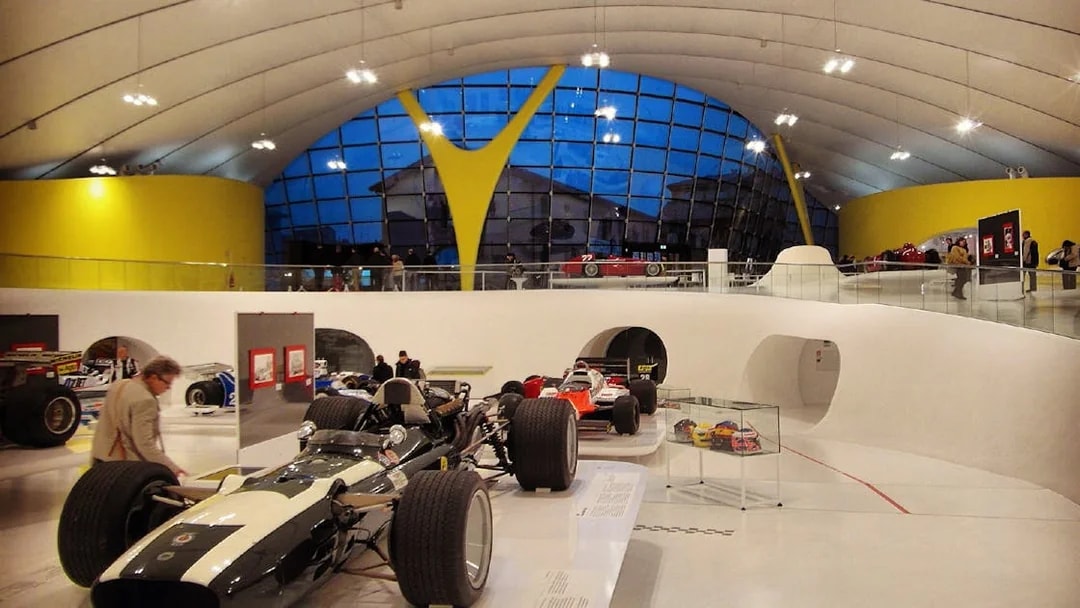 Race cars displayed inside Museo Enzo Ferrari Modena with modern architecture.