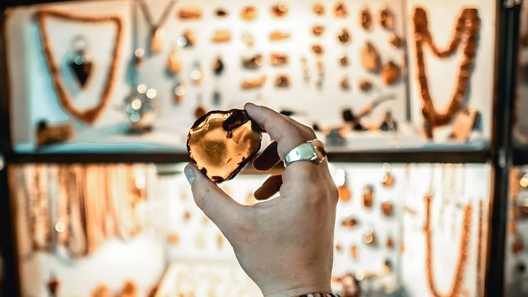Hand holding amber piece in Gdańsk workshop with jewelry display in background.