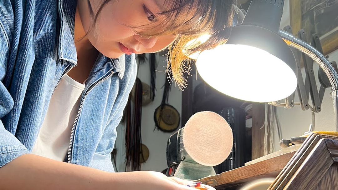 Person crafting amber jewelry under a lamp at Gdańsk Amber Workshop.