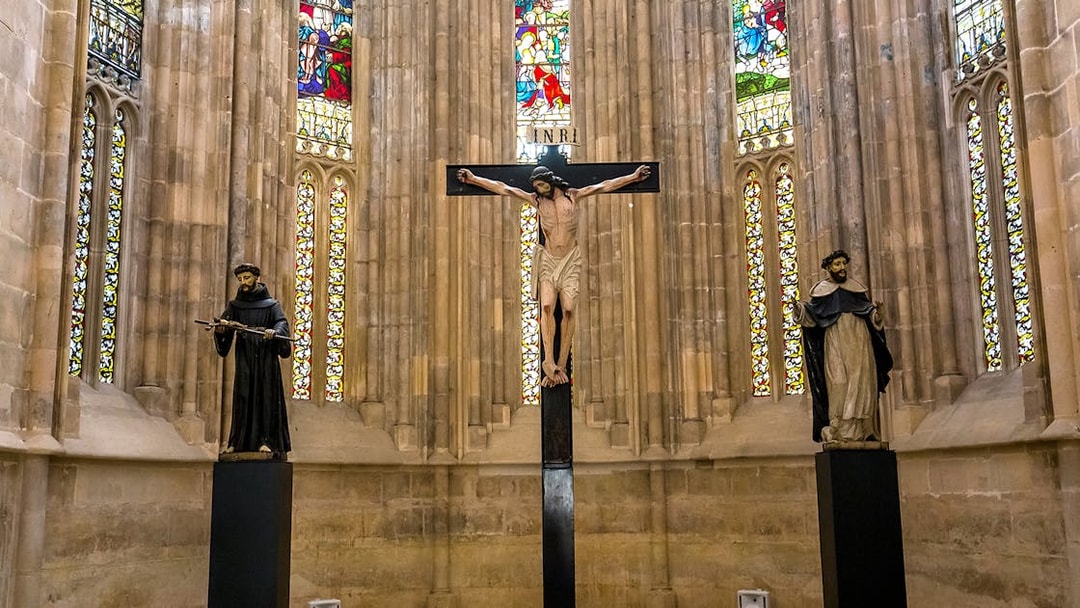 Crucifix and statues inside Batalha Monastery with stained glass windows.