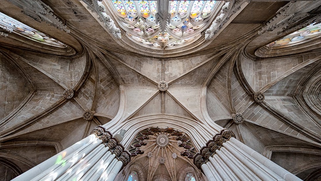 Batalha Monastery ceiling with intricate stone arches and stained glass windows.