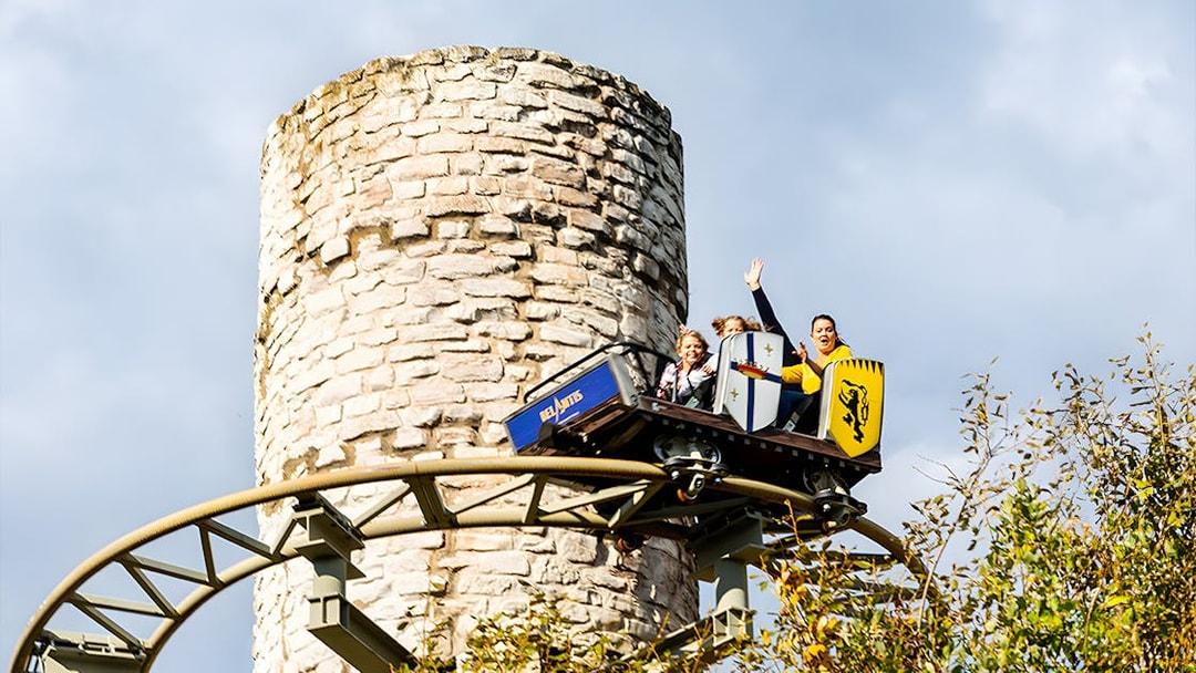 Roller coaster at Belantis Adventure Park with riders near a stone tower.