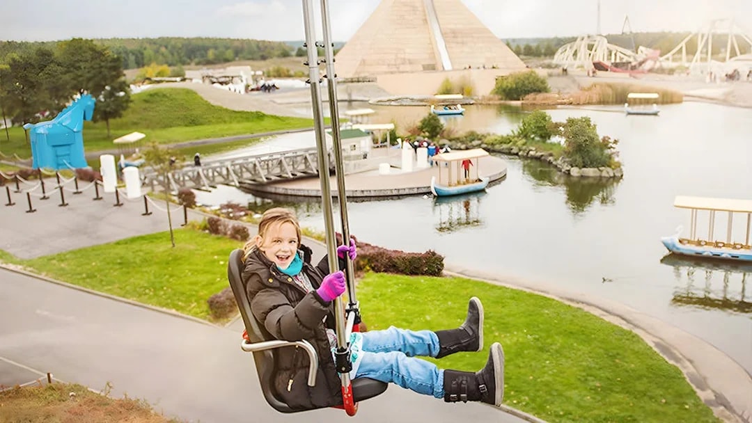 Child enjoying a ride at Belantis Adventure Park with pyramid and lake in background.