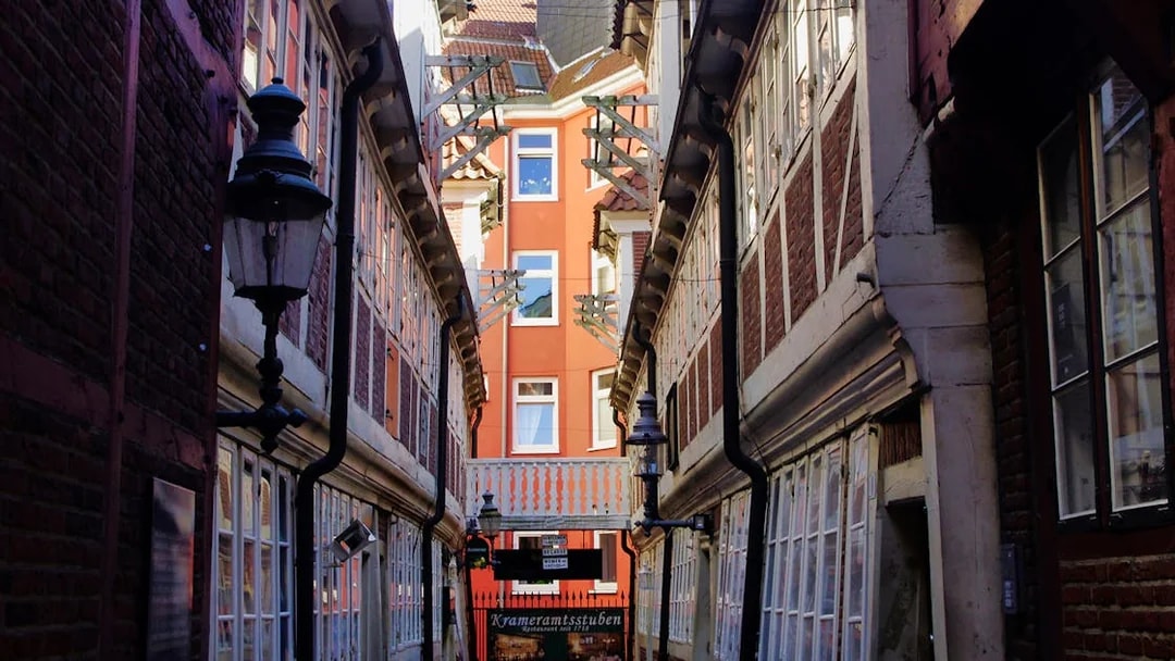 Narrow alleyway in Hamburg with historic brick buildings and Krameramtsstuben sign.