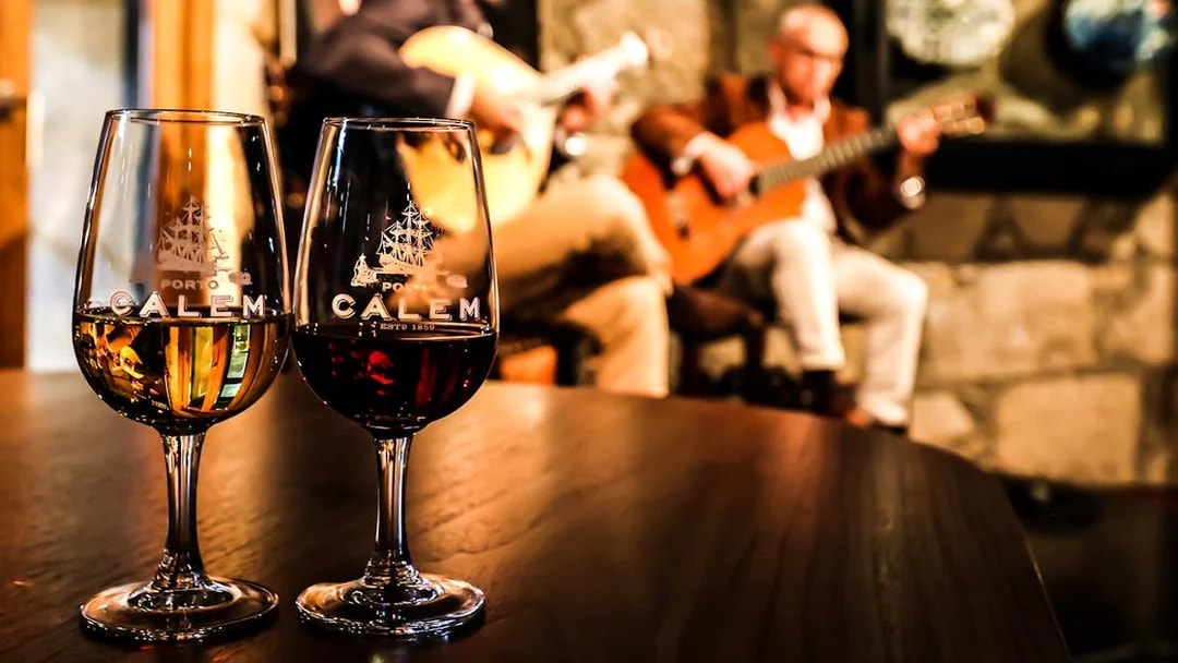 Fado musicians performing in a Port wine cellar with glasses of wine in the foreground.