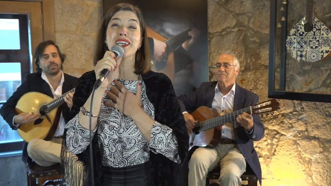 Fado singer performing with guitarists in a Port wine cellar concert.