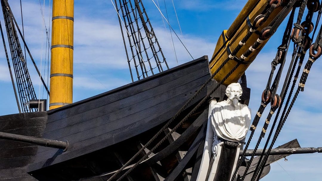 Frigate D. Fernando II e Glória bow with figurehead and rigging against blue sky.