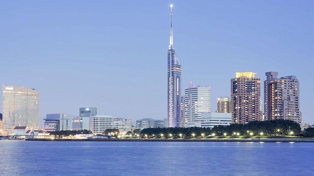 Fukuoka Tower illuminated at dusk with city skyline and waterfront.