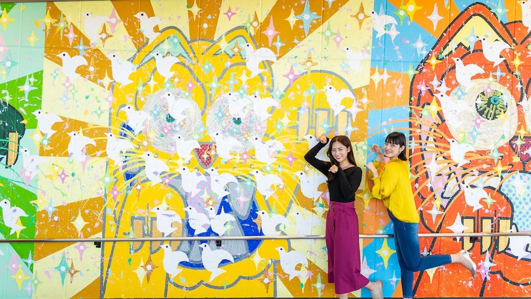 Colorful mural with doves at Hiroshima Orizuru Tower, featuring two people posing playfully.