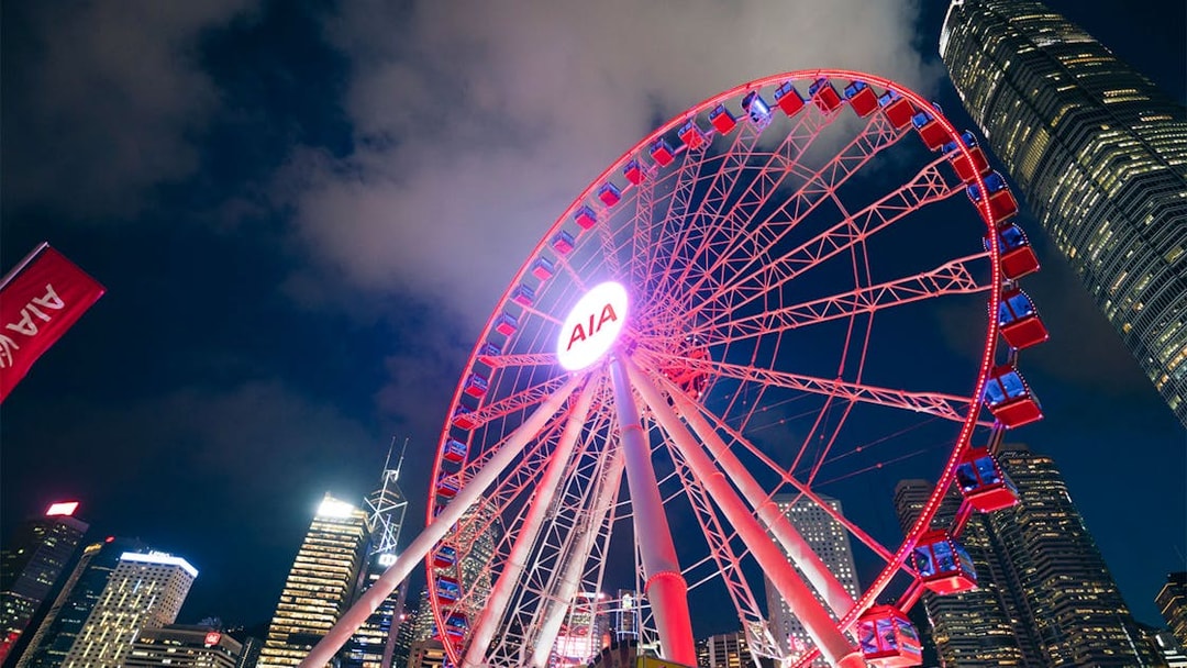 Hong Kong Observation Wheel illuminated at night with city skyline.