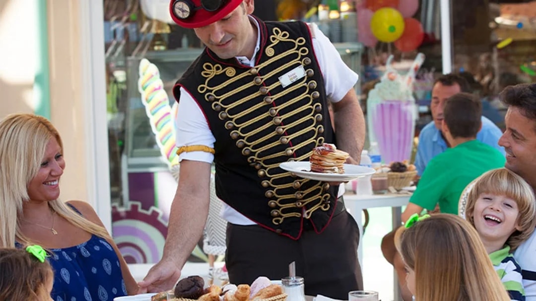 Server in themed attire serving food to a family at Katmandu Park.