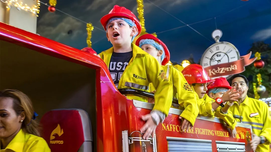 Kids in firefighter uniforms on a fire truck at Kidzania Abu Dhabi.