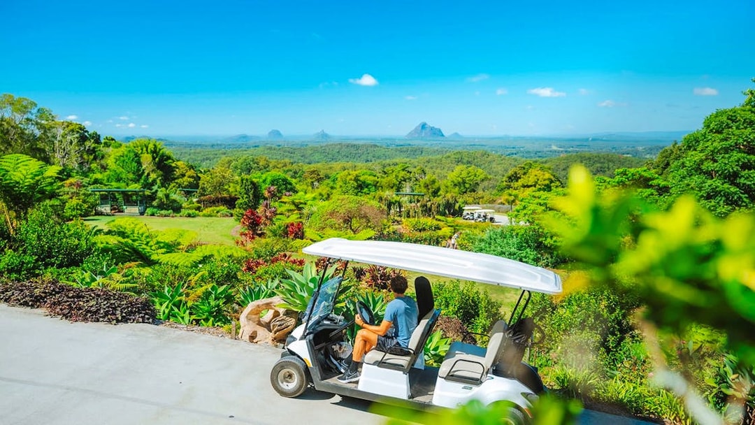 Golf cart driving through Maleny Botanic Gardens with scenic mountain view.