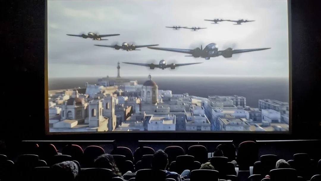 Audience watching Malta 5D show with planes flying over a cityscape.