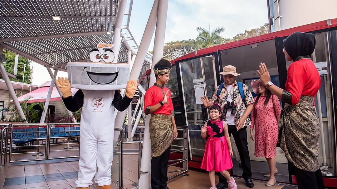 Visitors at Menara Taming Sari, Melaka, greeted by a mascot and staff in traditional attire.