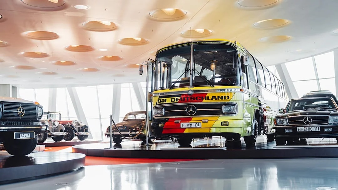 Mercedes Benz touring coach displayed in a museum setting with vintage cars.