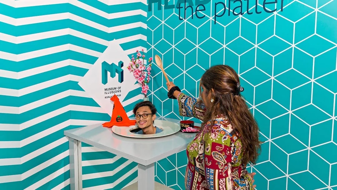 Person interacting with head-on-a-platter illusion at Museum of Illusions Kuala Lumpur.