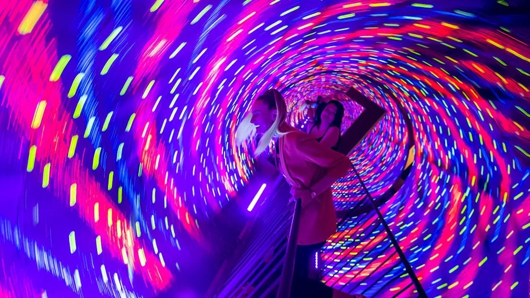 Visitors experiencing a colorful vortex tunnel with swirling lights.