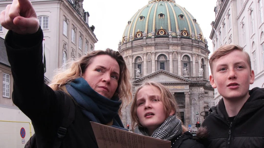 Mystery hunt participants at Amalienborg Palace, Copenhagen, pointing towards a landmark.
