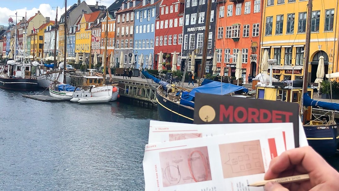 Nyhavn canal with colorful buildings and a person holding a mystery adventure booklet in Copenhagen.