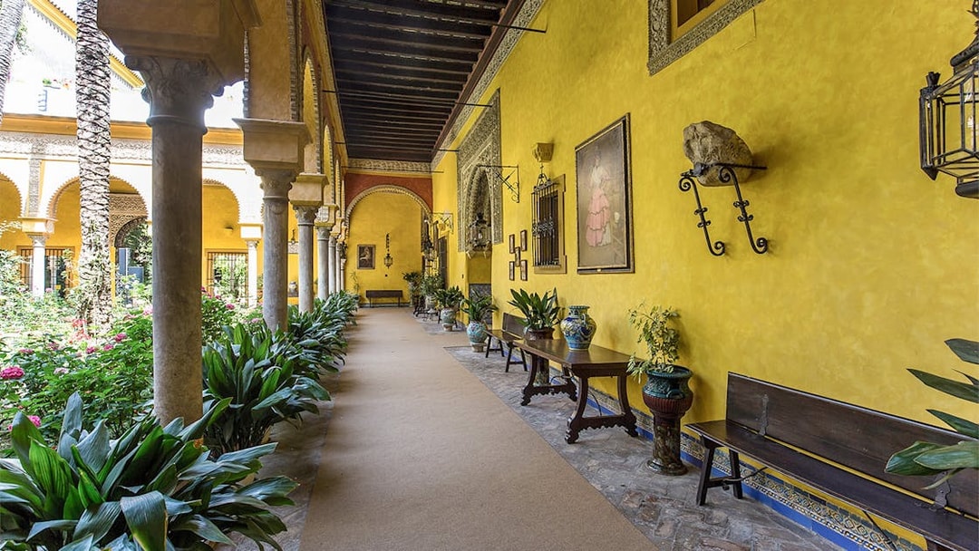 Palacio de las Dueñas courtyard with yellow walls, arches, and lush greenery.
