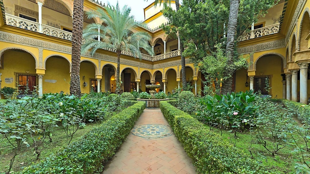 Palacio de las Dueñas courtyard with lush garden and central fountain in Seville.