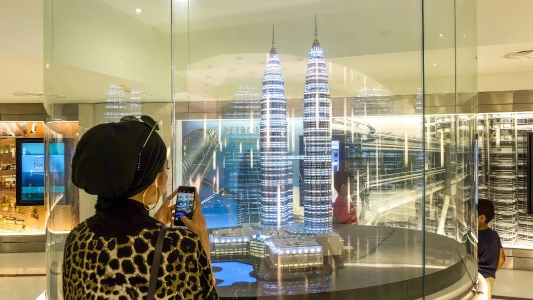 Visitor photographing Petronas Twin Towers model in Kuala Lumpur exhibit.