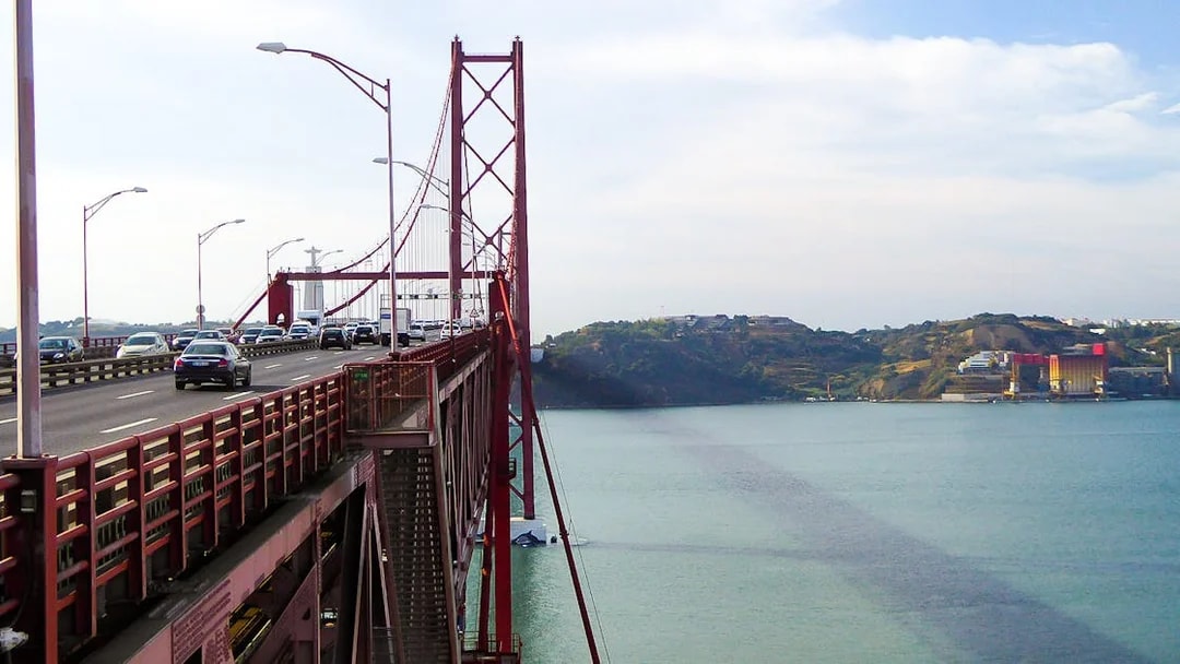 Cars crossing the 25 de Abril Bridge in Lisbon with Cristo Rei statue in the background.