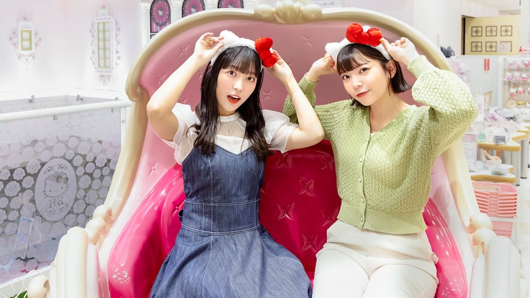 Visitors wearing Hello Kitty headbands at Sanrio Puroland, seated on a themed bench.