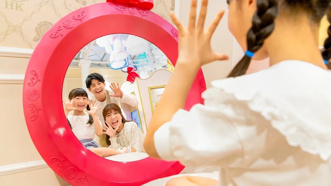 Family posing in a Hello Kitty-themed mirror at Sanrio Puroland.