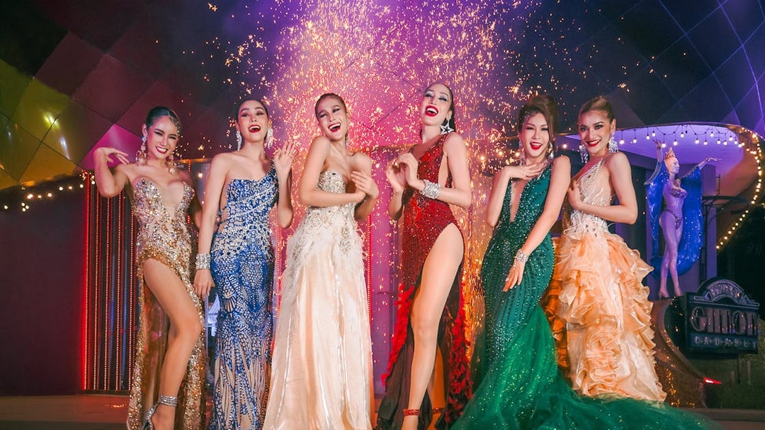 Performers in vibrant costumes at Simon Cabaret Show, Phuket, with fireworks in the background.