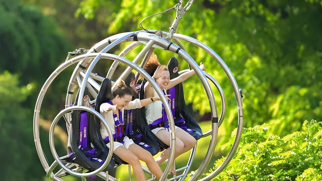Two people enjoying the Slingshot ride in Singapore amidst lush greenery.