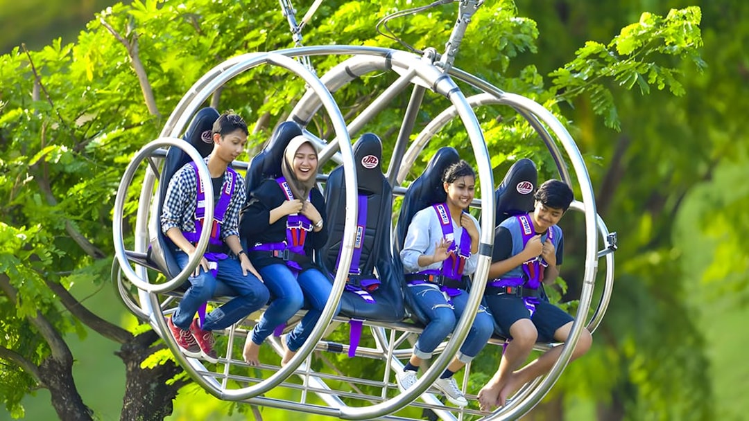 People enjoying the Slingshot ride in Singapore amidst lush greenery.