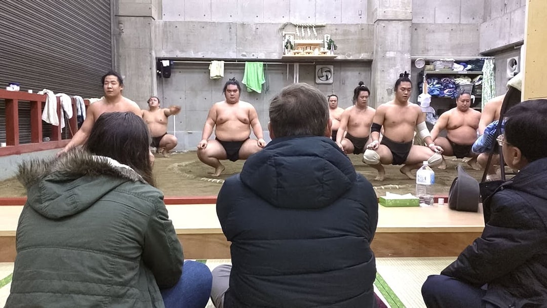 Sumo wrestlers training in a Tokyo dojo with spectators watching.