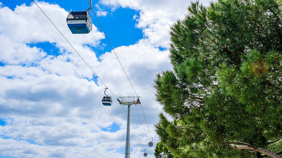 Telecabine cable cars in Lisbon, Portugal, gliding over trees and blue sky.