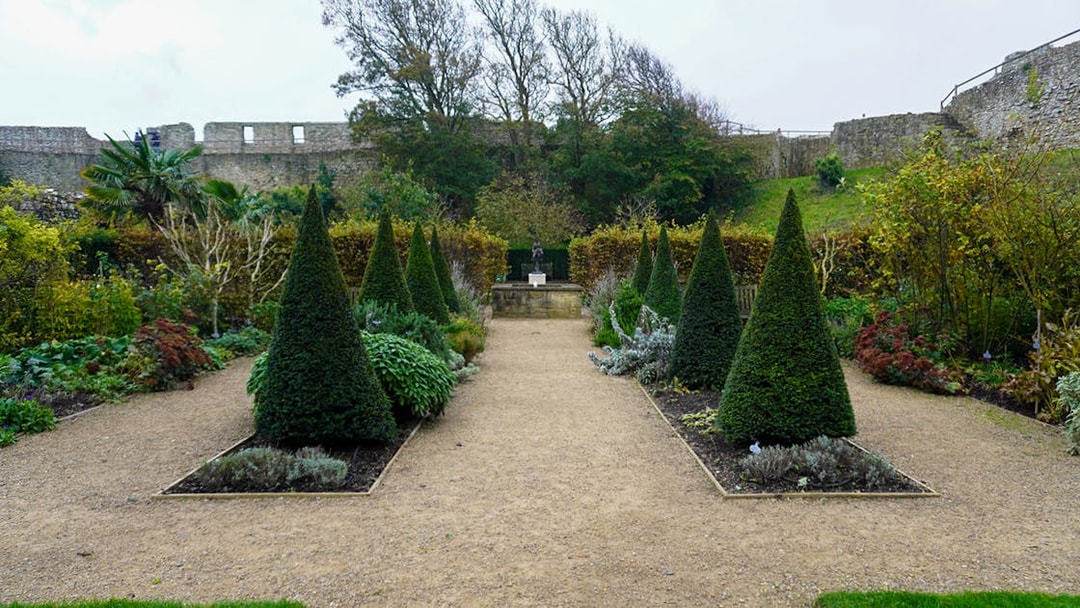 Carisbrooke Castle garden with topiary trees and stone walls in the background.