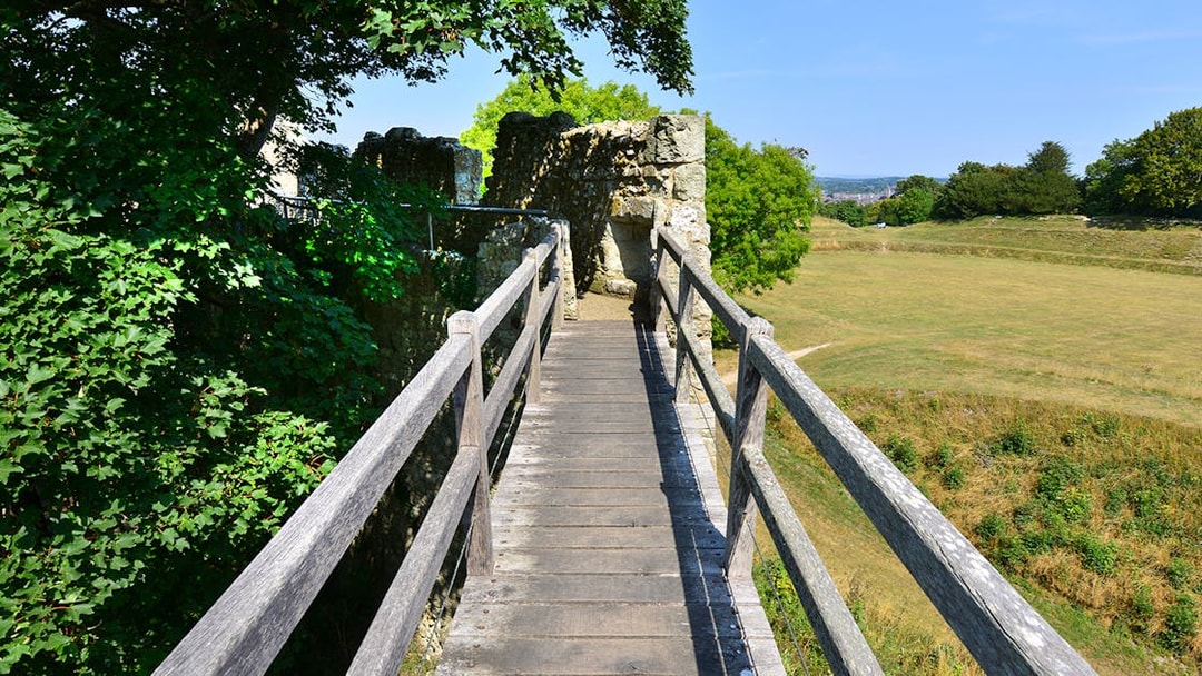 Walkway leading to Carisbrooke Castle ruins surrounded by greenery.
