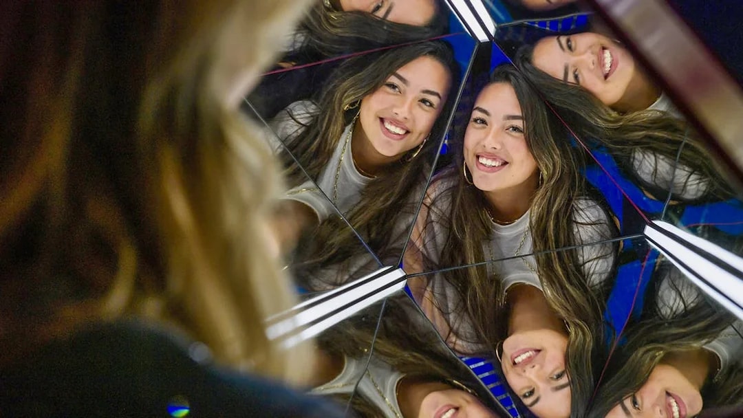 Reflections of a smiling woman in a mirrored exhibit at The TUBE.