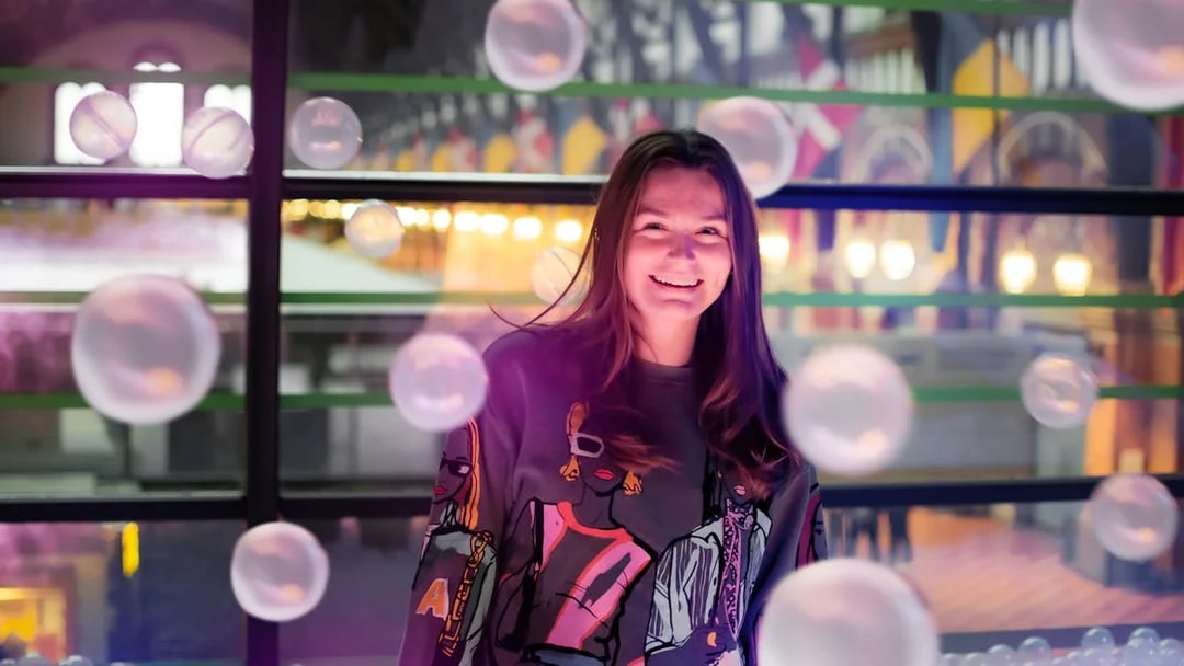 Person smiling inside The TUBE in Copenhagen with colorful lights and bubbles.