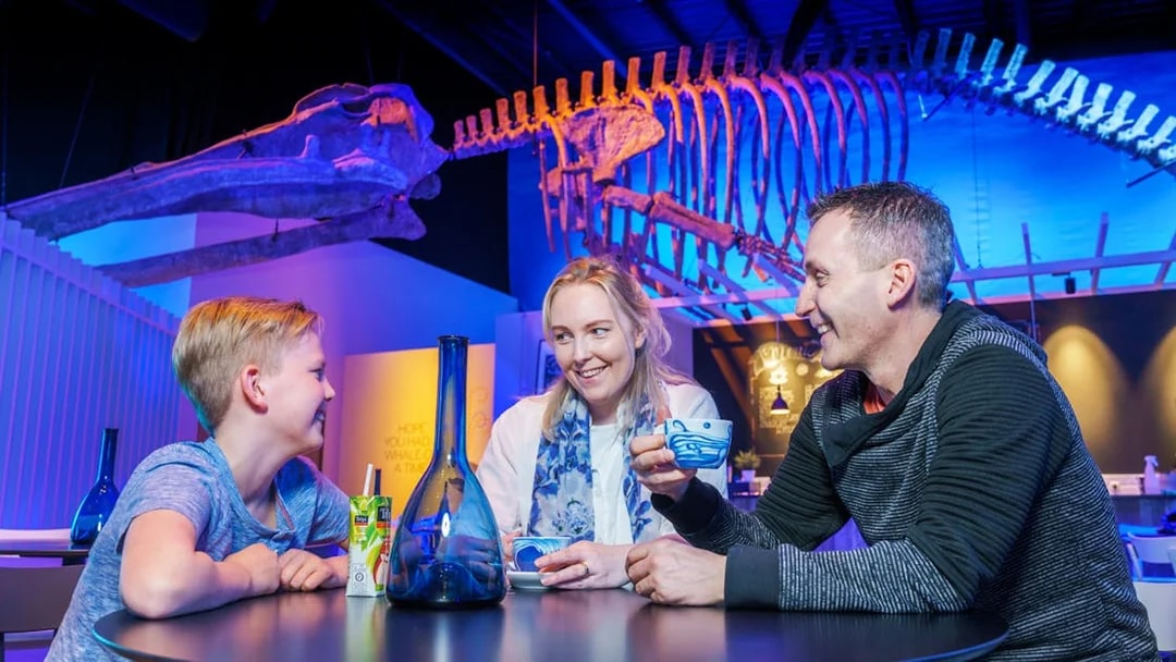 Family enjoying drinks under whale skeleton at Whales of Iceland Museum.