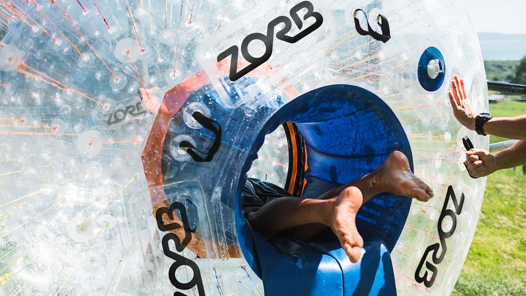 Person entering a Zorb inflatable ball for a ride on a grassy hill.