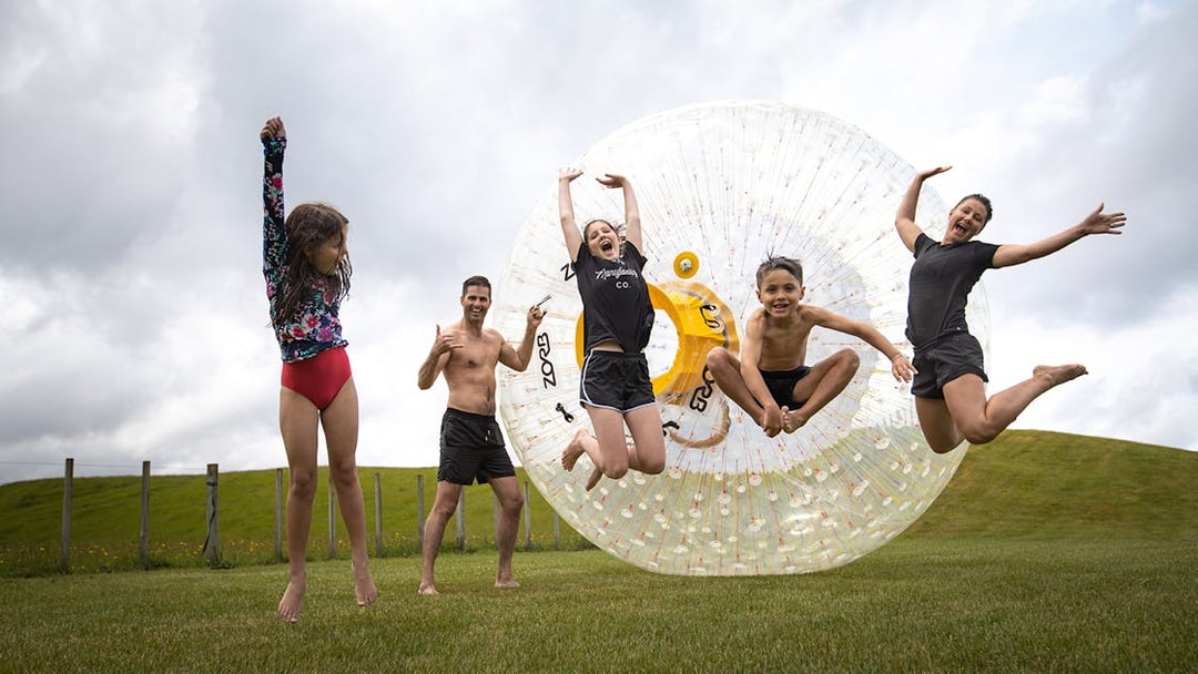 Group enjoying Zorb giant inflatable ball ride on grassy hill.