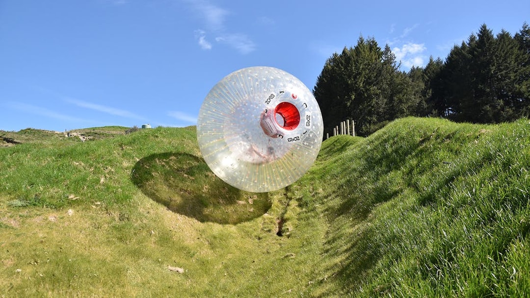 Zorb ball rolling down a grassy hill under a clear blue sky.