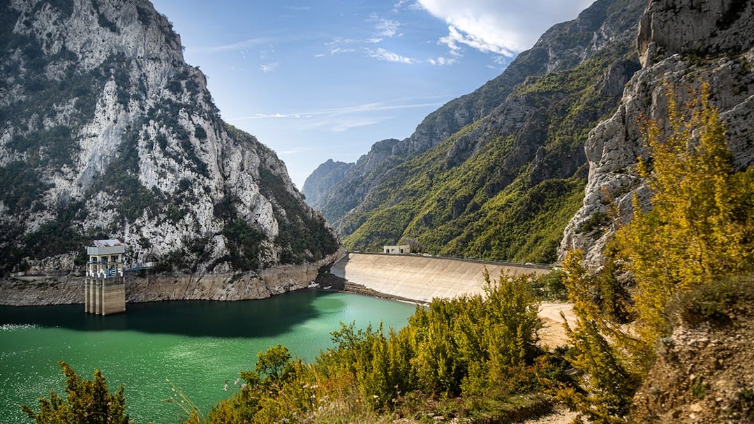 Bovilla Lake dam reservoir surrounded by rocky mountains and green foliage.