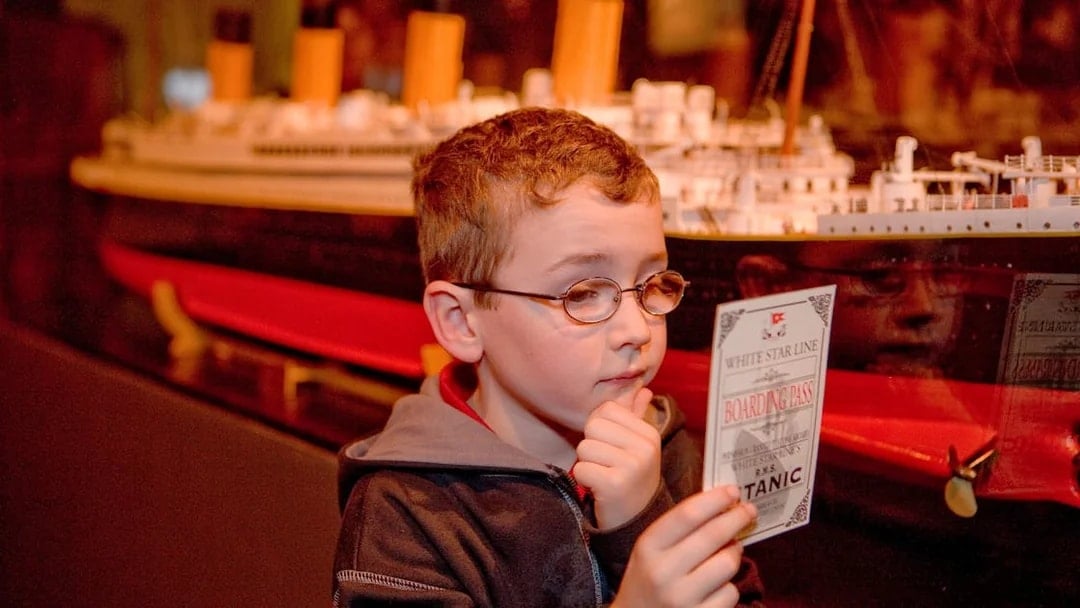 Child examining Titanic boarding pass at artifact exhibition.