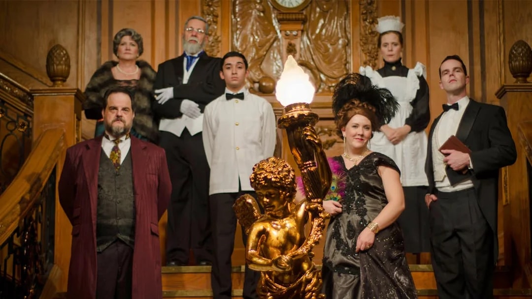 Group in period costumes on Titanic's grand staircase at artifact exhibition.